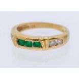 An emerald and diamond ring, comprising a central channel set row or three round mixed cut emeralds,