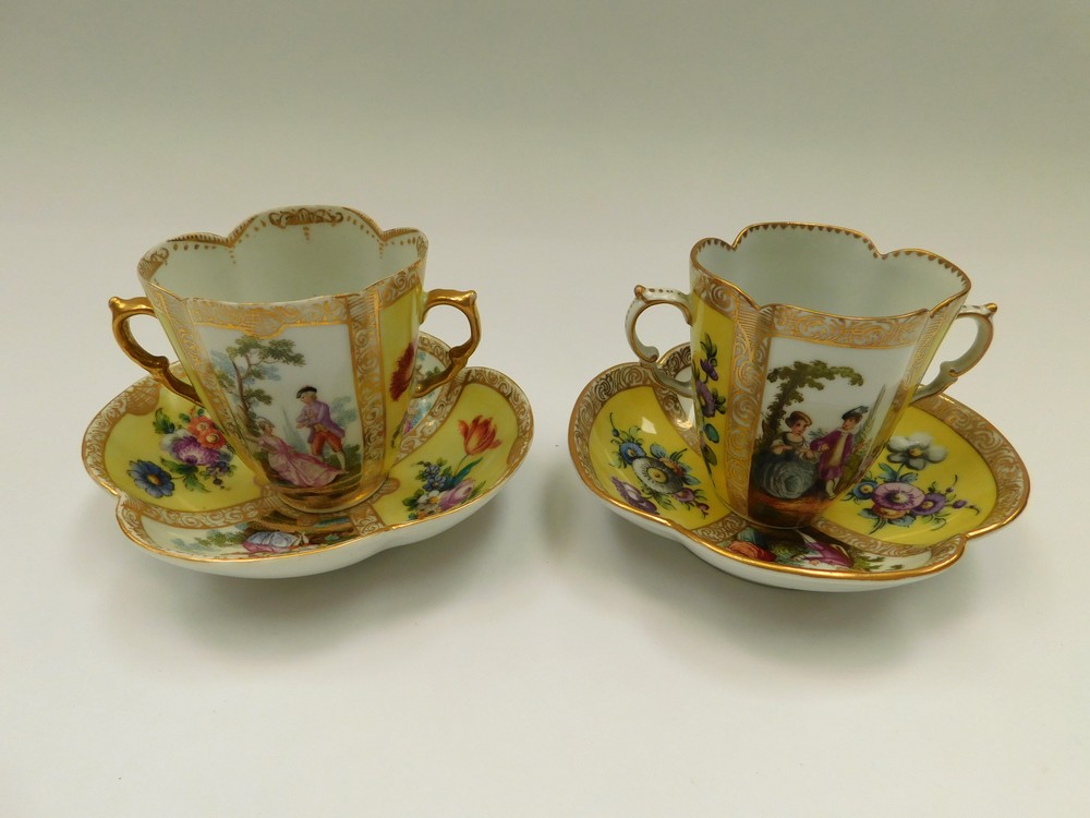 Two Dresden quatrefoil twin-handled chocolate cups and saucers, with two yellow ground panels