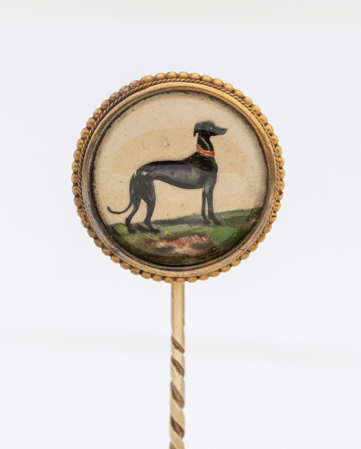 An Essex crystal gold stick pin, comprising a round crystal depicting a Greyhound, within a beaded