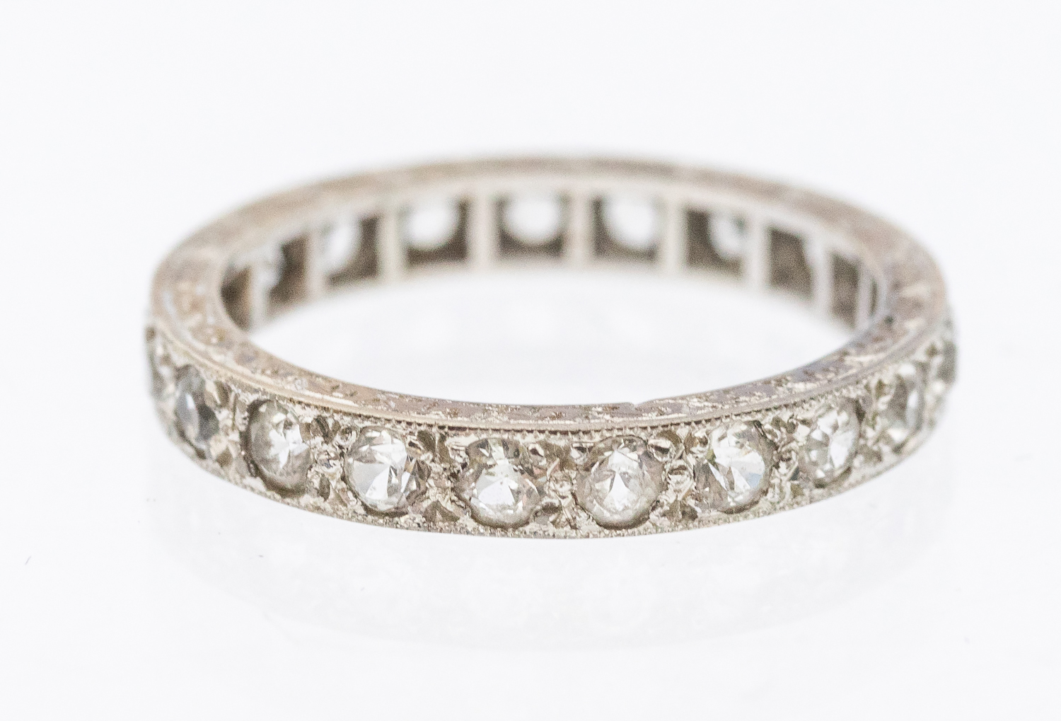 A stone set white metal eternity ring, width approx 3mm, size K1/2, unmarked, engraved mount,