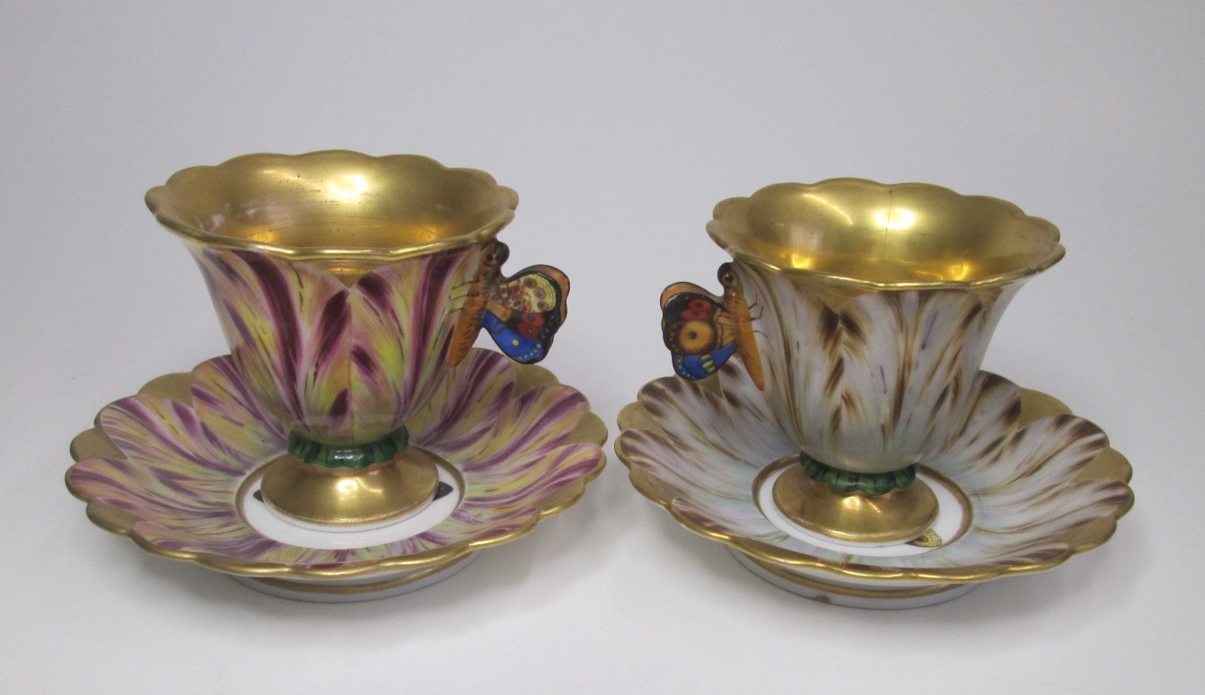A pair of Continental cups and saucers with butterfly handles and the saucers decorated with