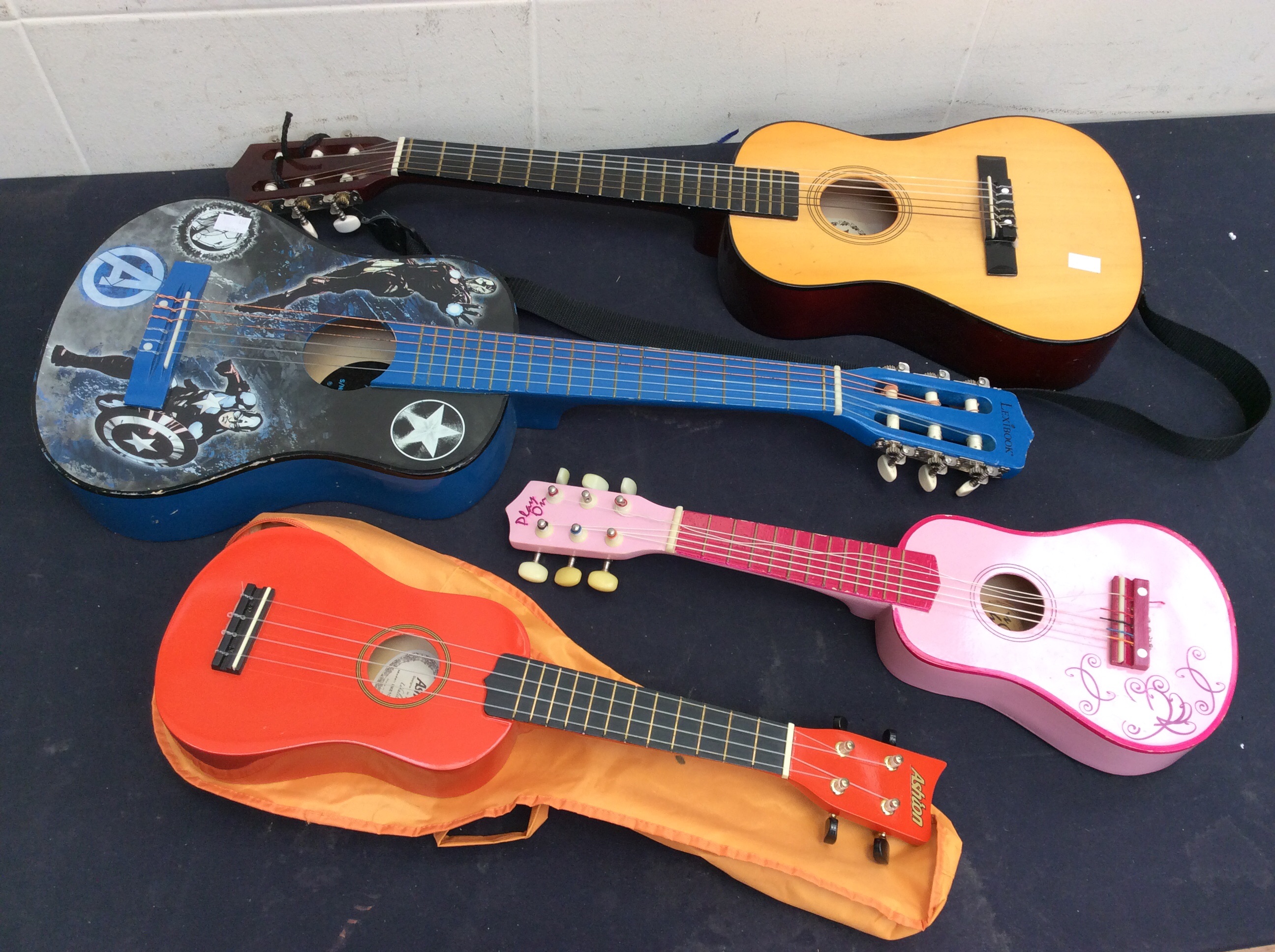 Two children's guitars along with two other smaller instruments.