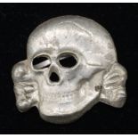 A Totenkopf metal SS skull, non maker marked. Brass alloy base metal, with silver wash, and 2 folded