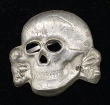 A Totenkopf metal SS skull, non maker marked. Brass alloy base metal, with silver wash, and 2 folded