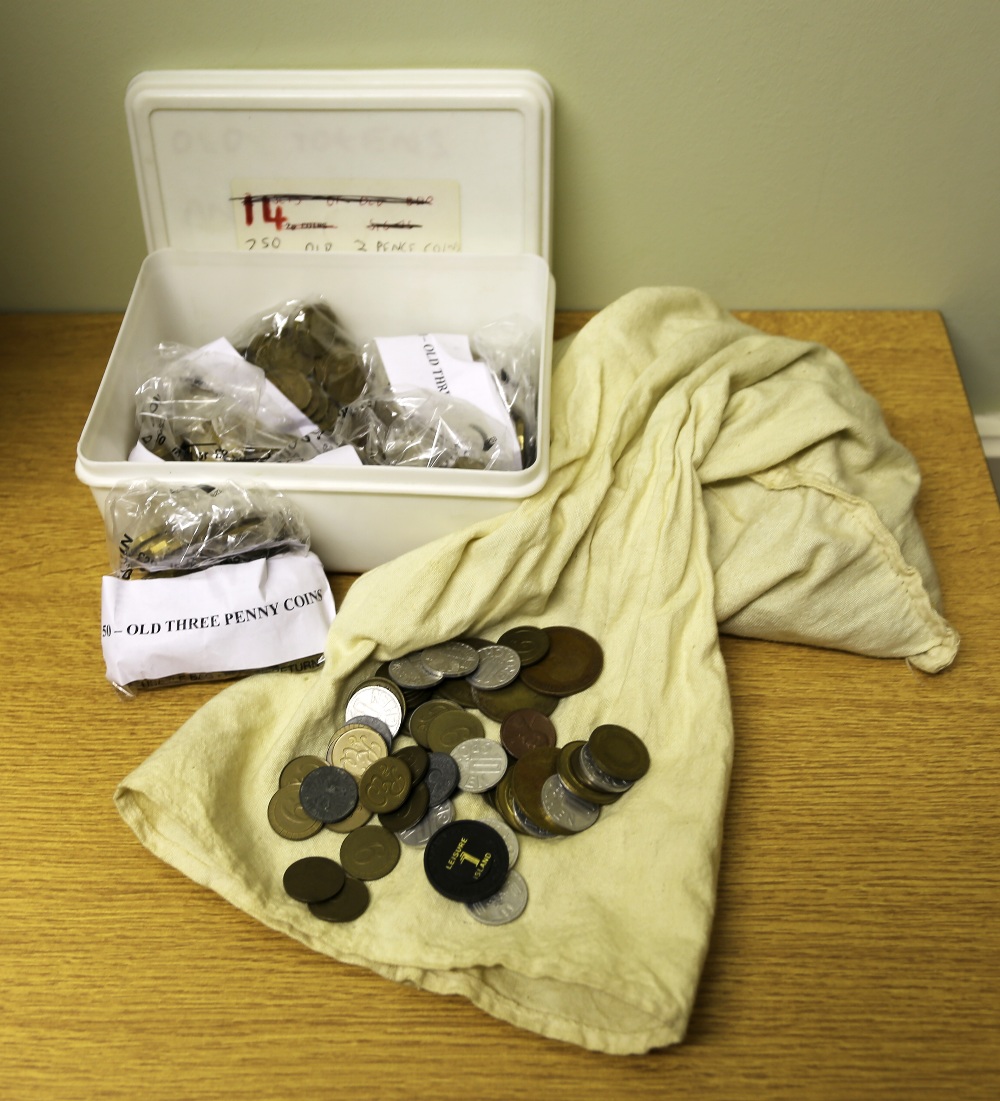 A collection of old threepence coins and slot machine tokens used for amusement machines. One box