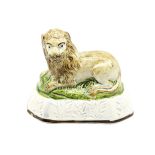 A pearlware model of a recumbent lion laying on a grassy mound on a base with moulded relief.  Circa