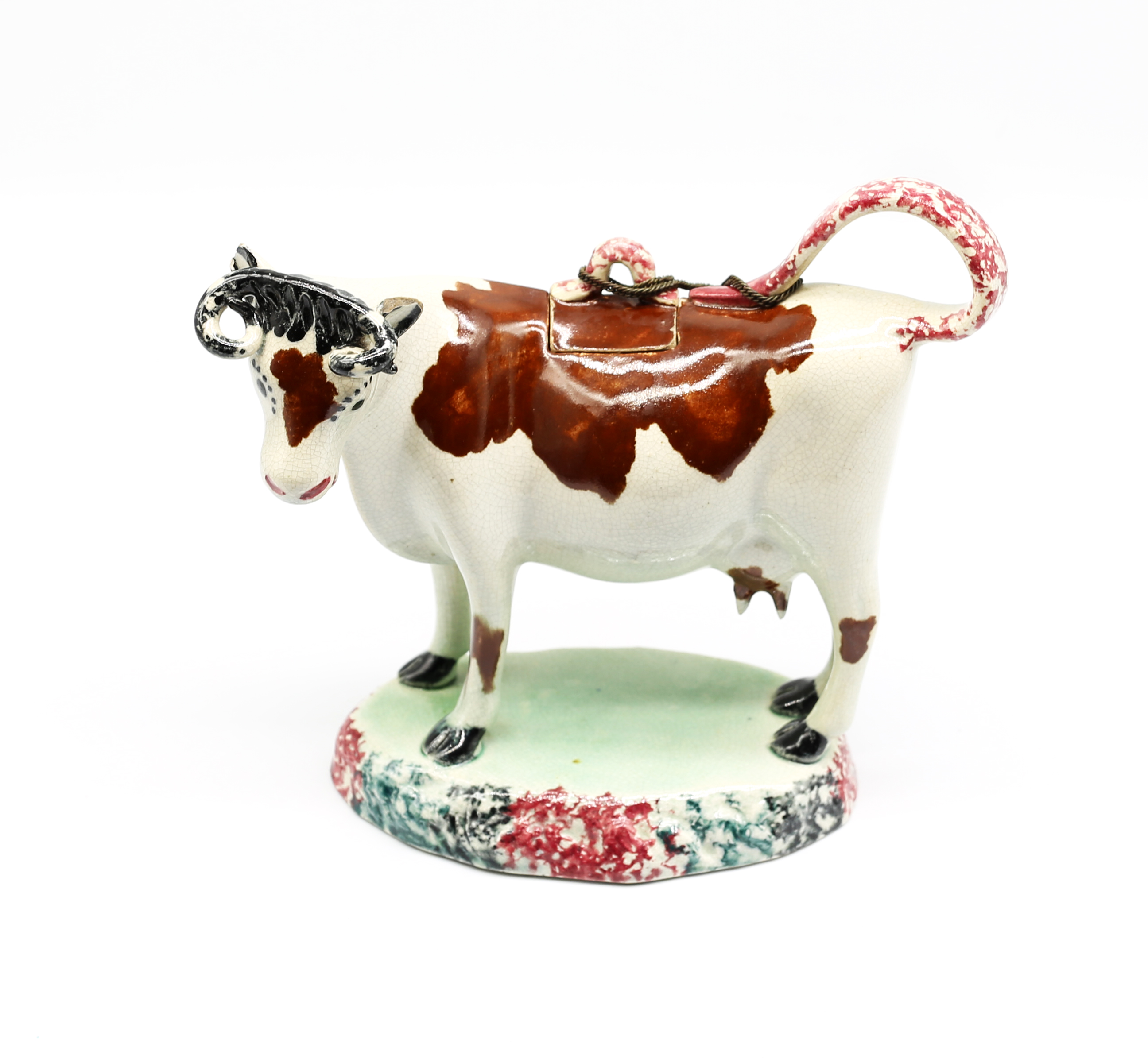 A North country pottery cow creamer and cover, standing on a green base with a mottled coloured base