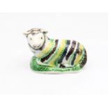 A pottery model of a recumbent Ewe, decorated with green, yellow and black stripes.  Circa 1800-