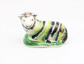A pottery model of a recumbent Ewe, decorated with green, yellow and black stripes.  Circa 1800-