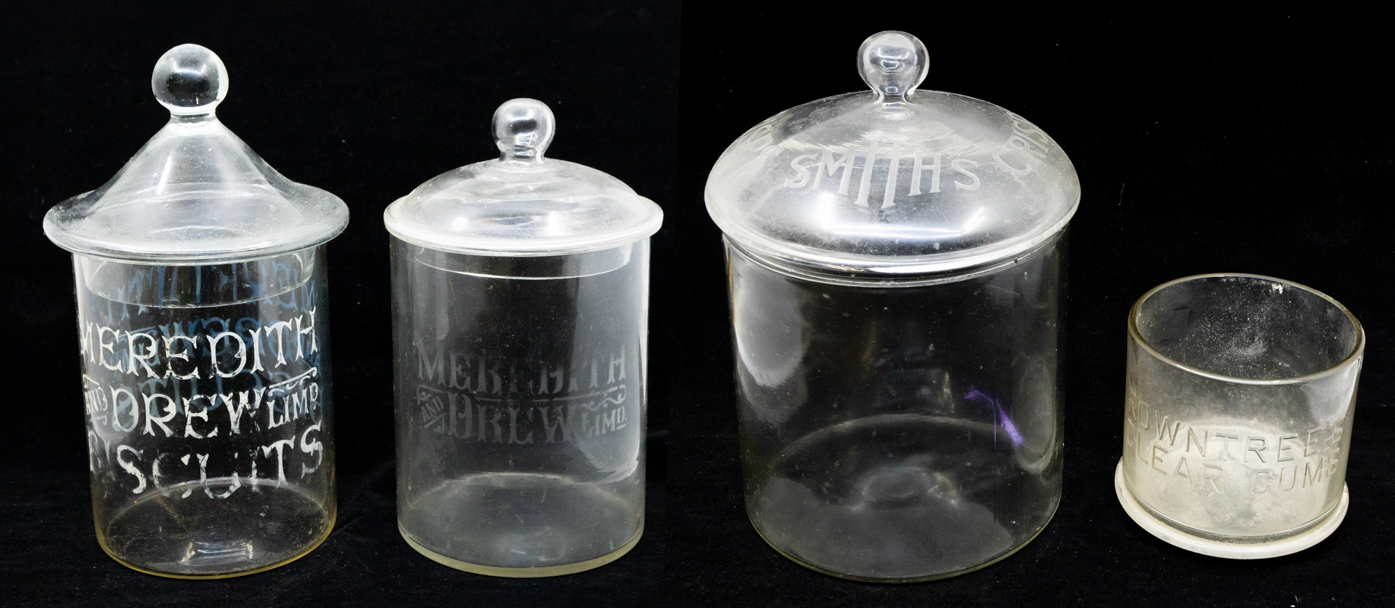 A collection of early 20th Century glass advertising jars, four in all, three with lids, Meredith