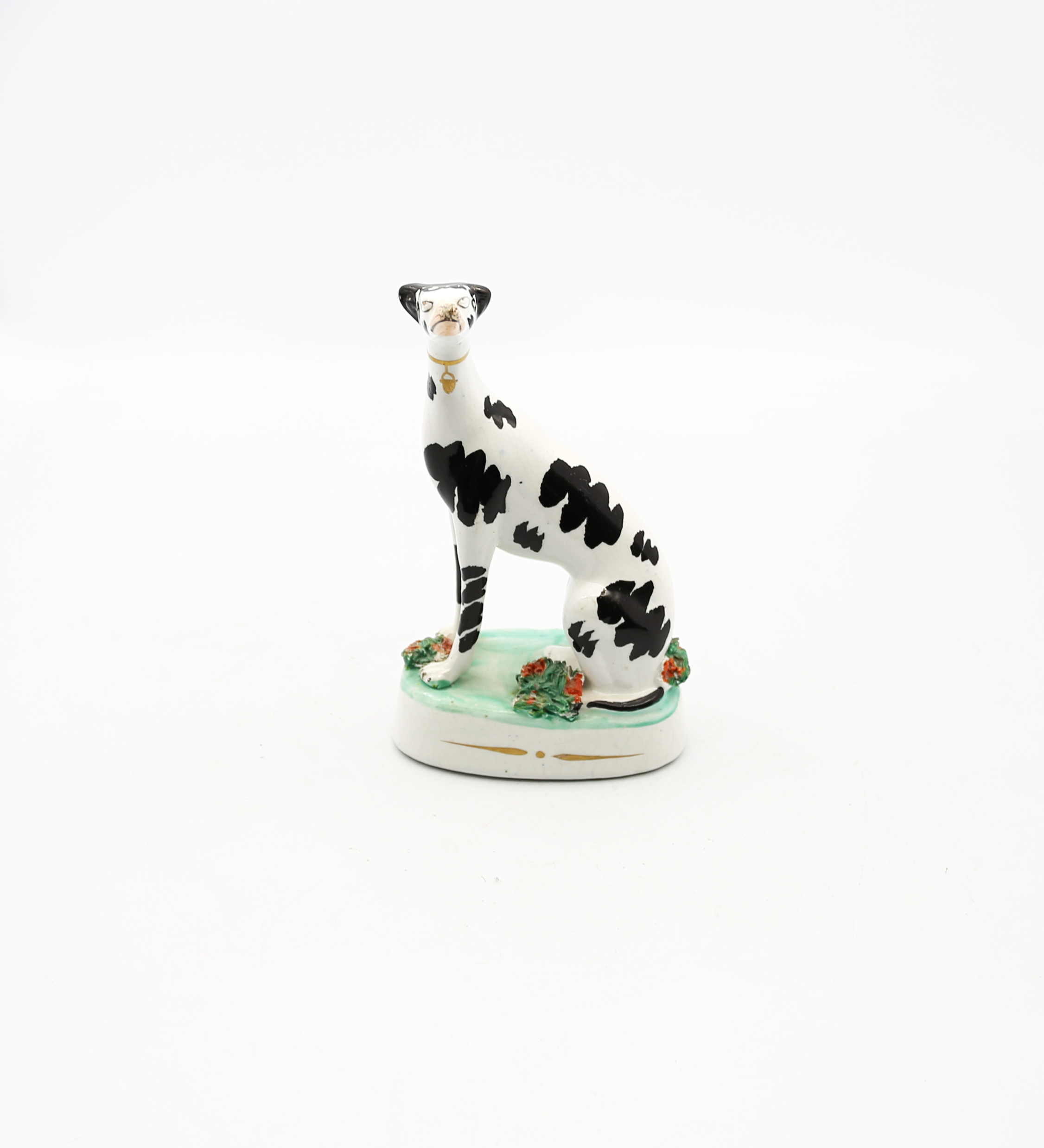 A Staffordshire potter model of a seated black and white Dalmatian on a green oval base.  Circa