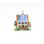 A small Prattware money box in the shape of a house, flanked with a man and woman on either side.