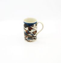 A slipware cylindrical mug in a blue, brown, black and and white marbling with a blue band to the