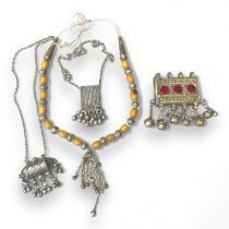 A collection of white metal Bedouin jewellery. Comprising a  glass panel set amulet, an amber type