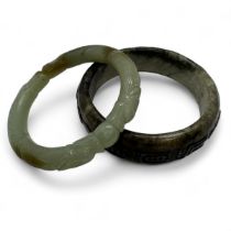 Two carved nephrite jade Chinese bangles. One featuring carved characters, the other featuring two