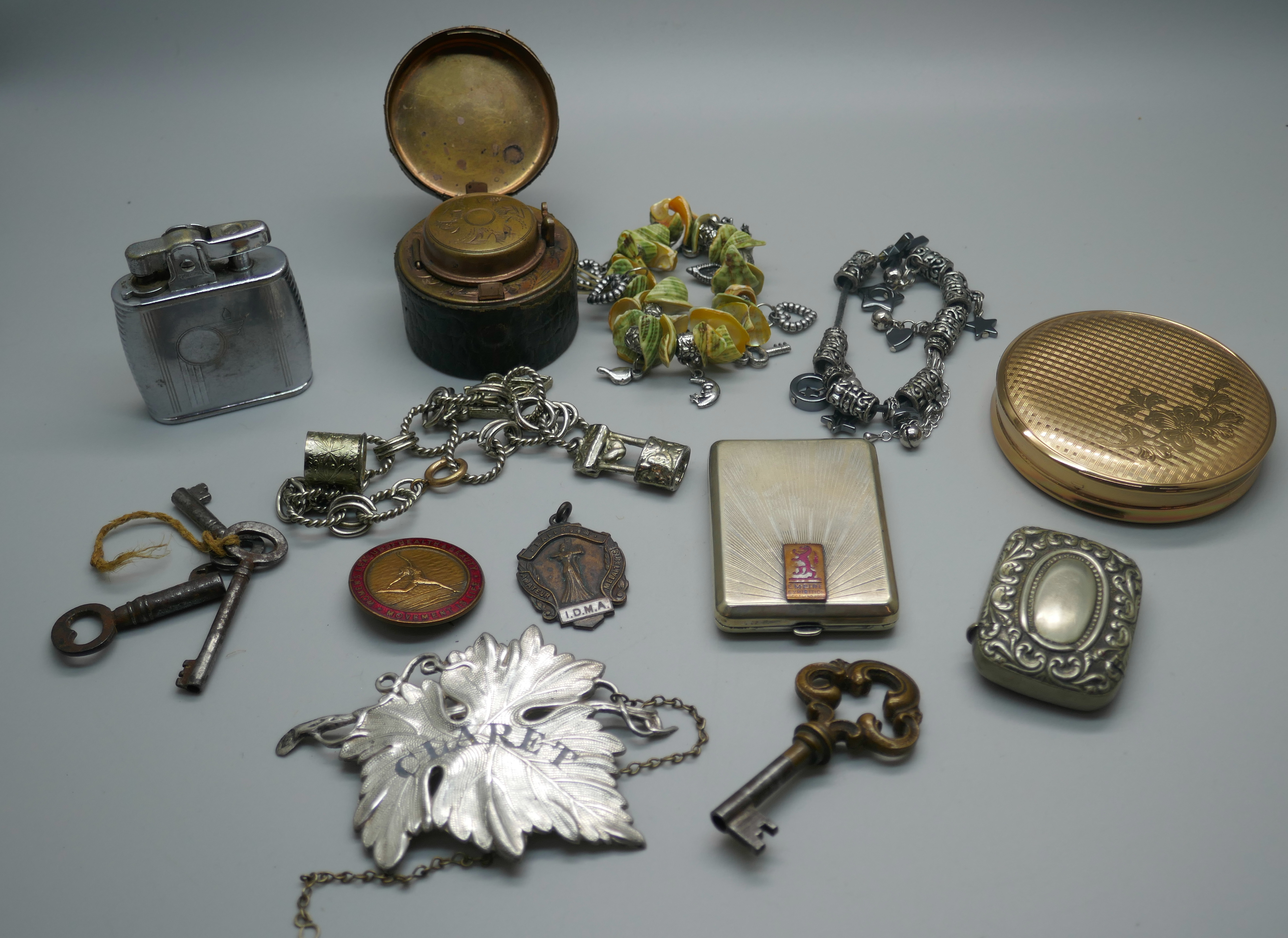 A powder case, a claret decanter label, an inkwell, a lighter, three bracelets with charms, a