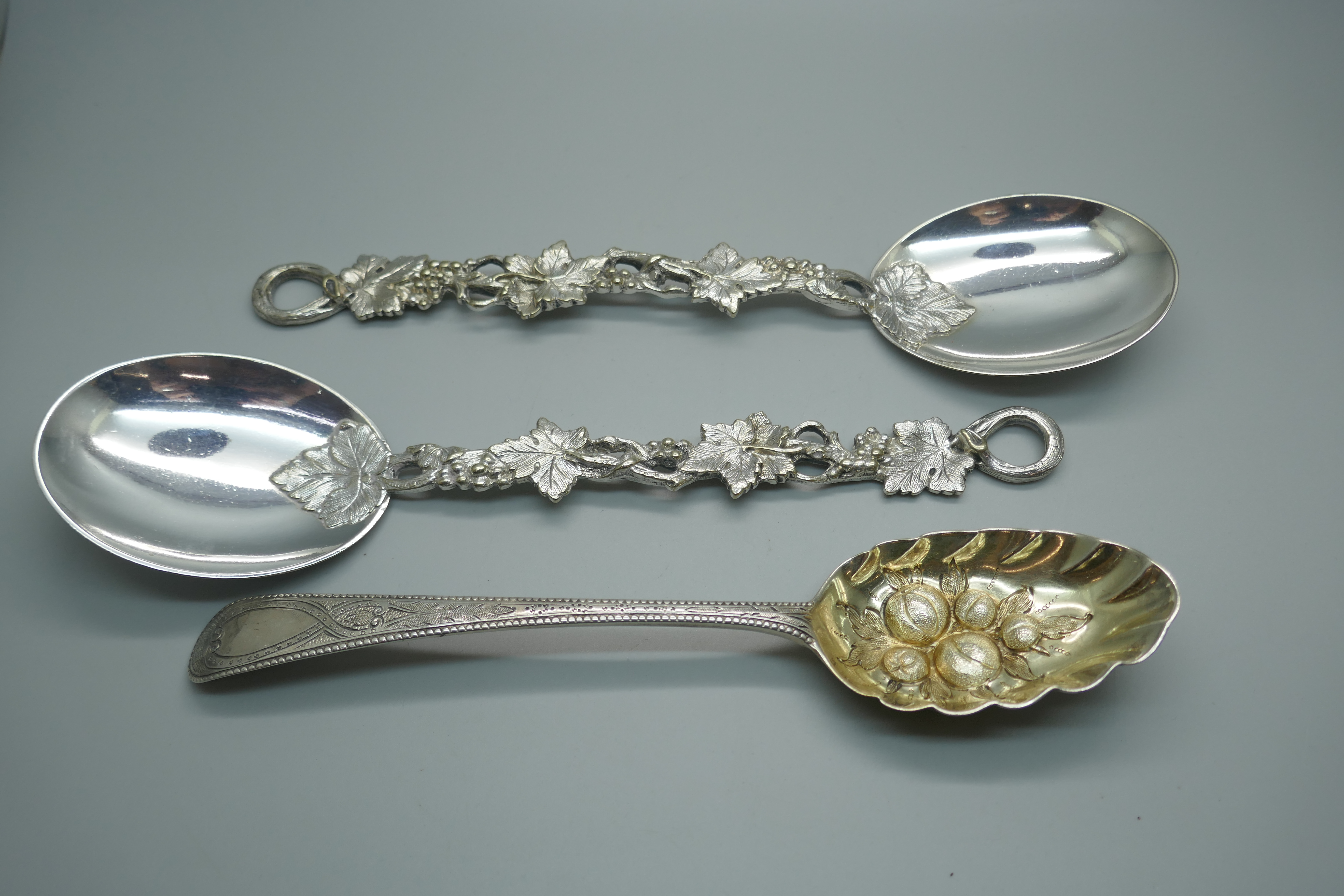 A George III silver berry spoon, London 1782, 65g, and two vine detail serving spoons