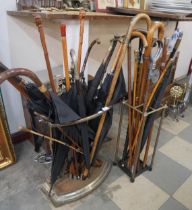 A cast iron stick stand and one other, and a large collection of walking sticks and umbrellas