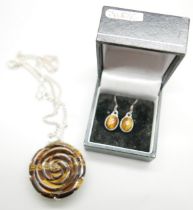A carved silver mounted tigers eye pendant on a silver chain and a pair of tigers eye earrings,