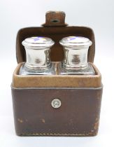 A pair of perfume bottles with enamelled tops in a leather travel case