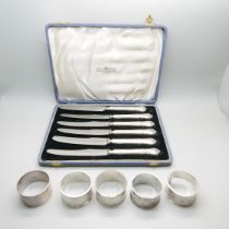 Five silver napkin rings, one a/f, 134g, and six silver handled knives with later replacement blades