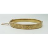 A 9ct yellow gold bangle with engraved front and safety chain, 9.9g