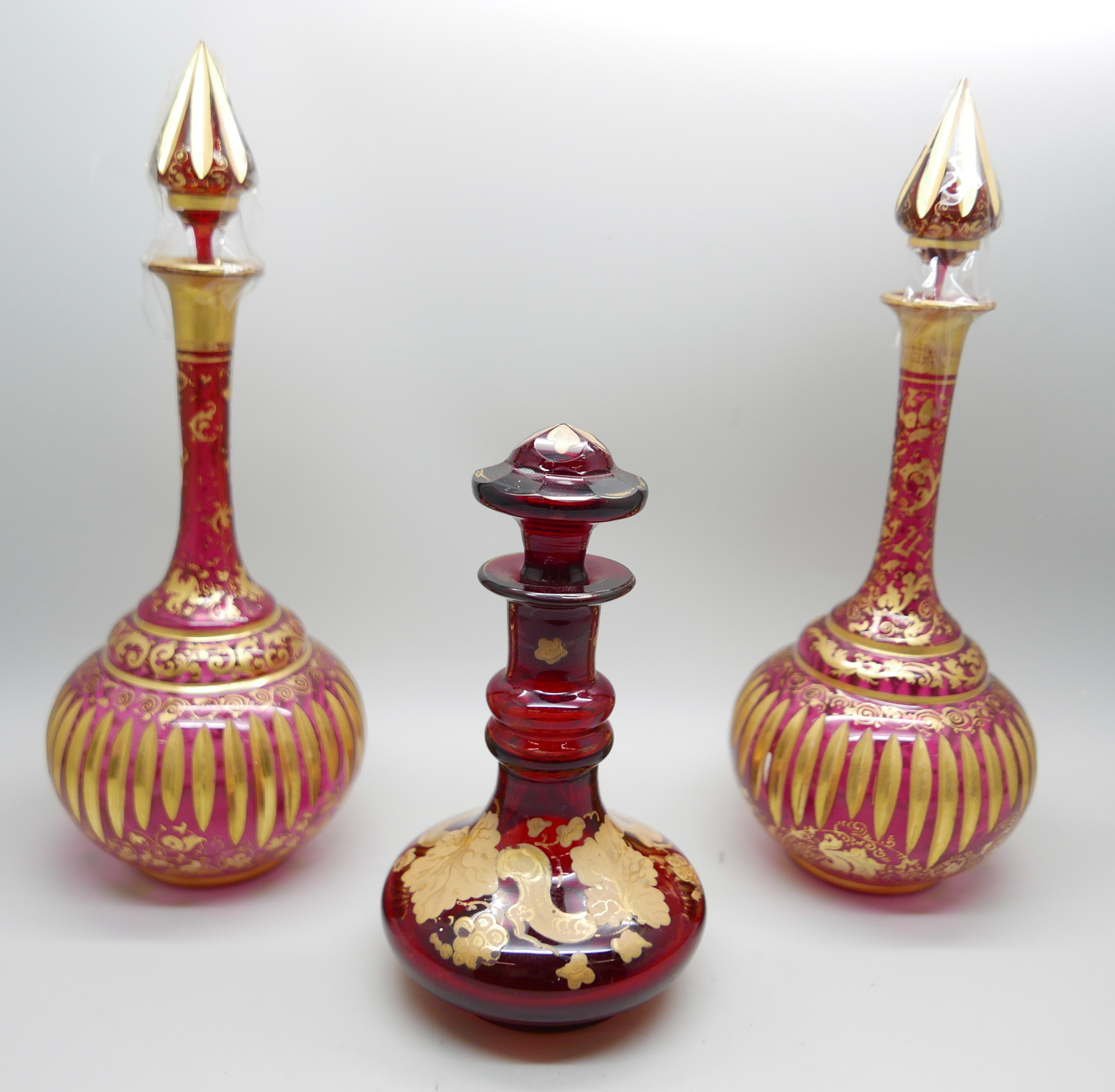 A pair of early 20th Century cranberry glass bottle with lids and gilt detail and a ruby glass scent