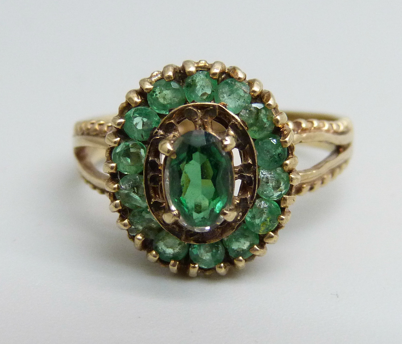 A 9ct gold ring, set with a green centre stone and surrounded by fourteen emeralds, 3.3g, O