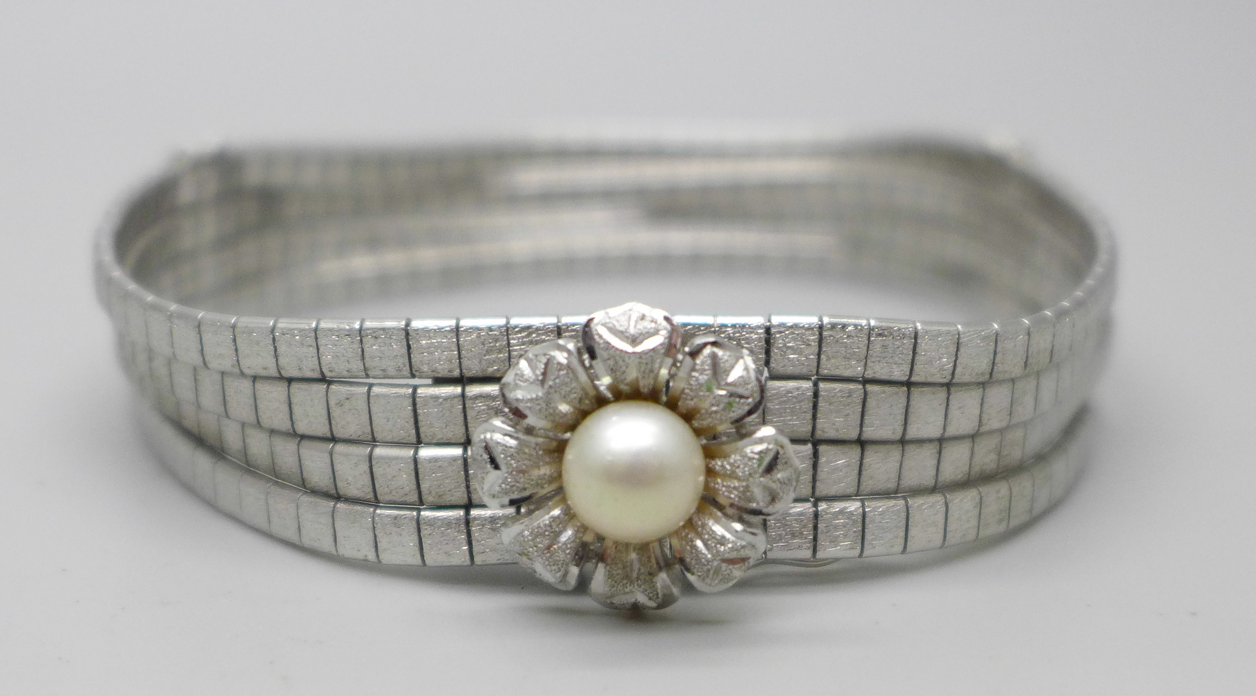 An articulated four row white metal bracelet with faux pearl centre flower fastener and safety