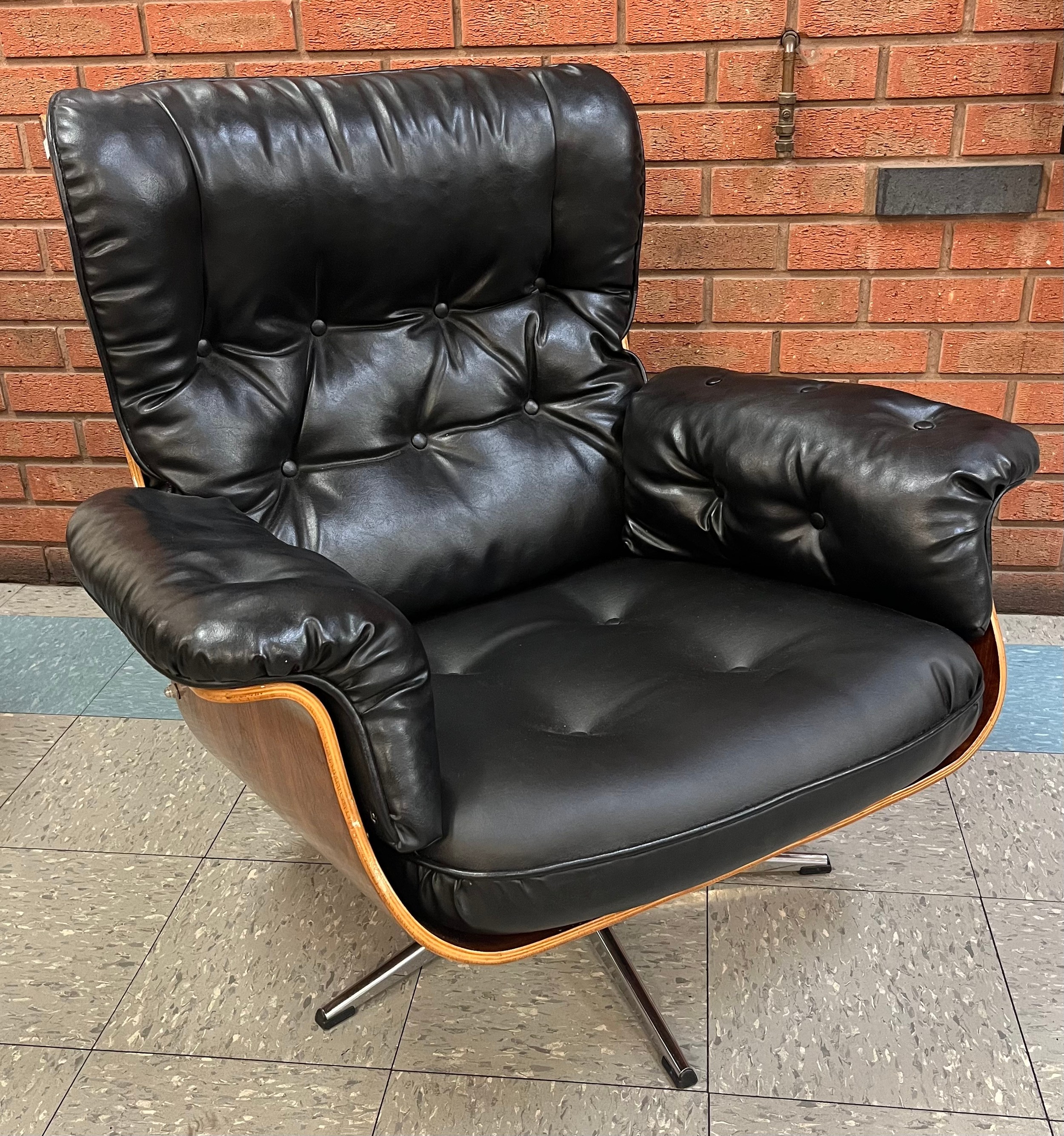 An Eames style simulated rosewood and black vinyl revolving armchair, on chrome base