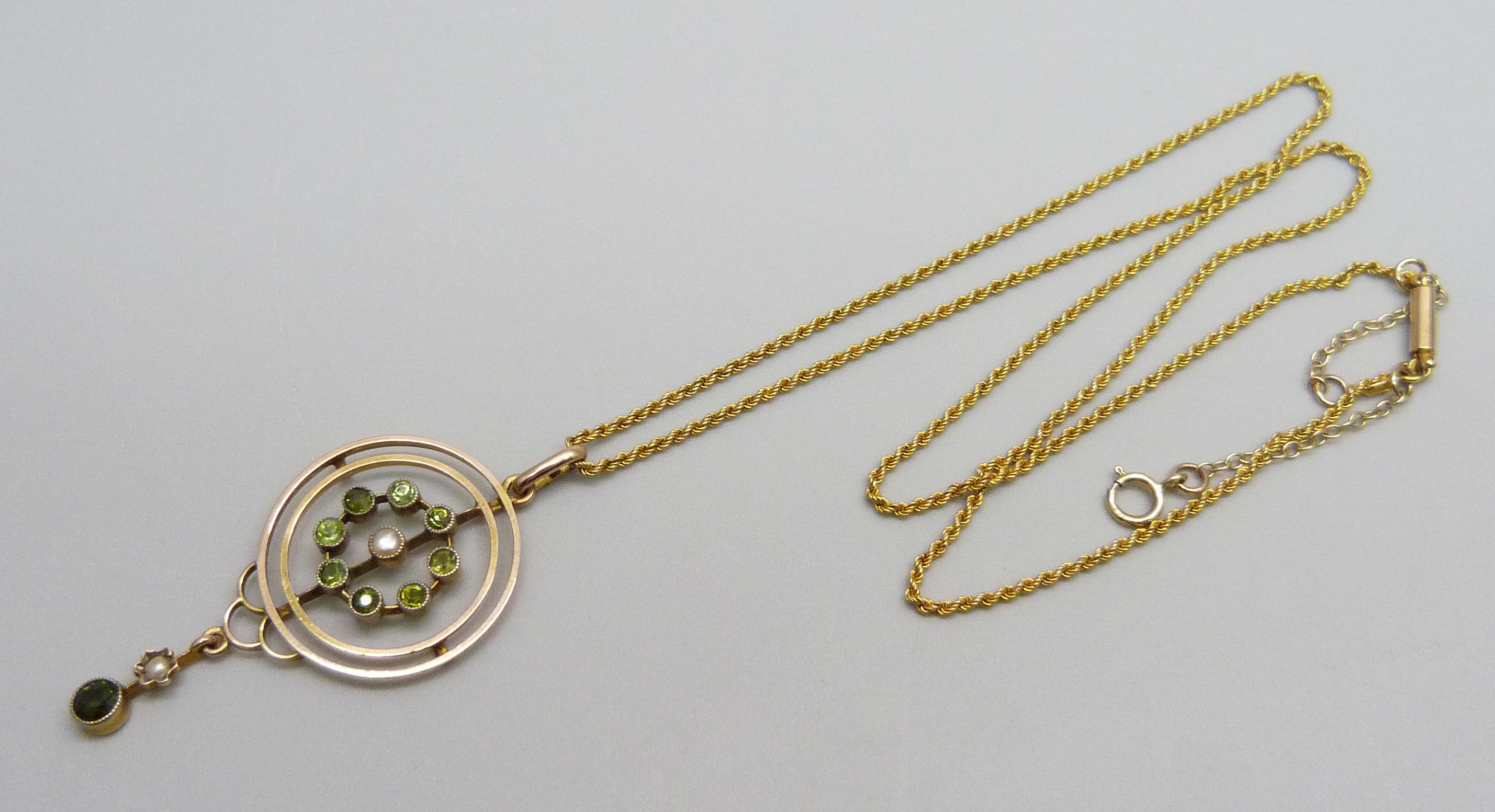 A 9ct gold Edwardian drop pendant set with eight peridot stones and a central seed pearl with a