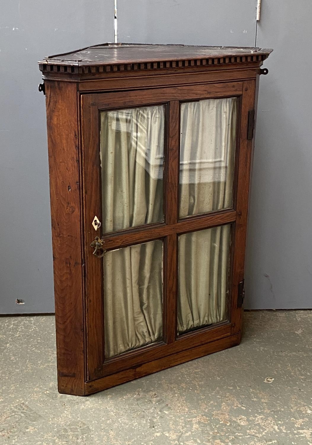 A George III oak corner cupboard, dentil cornice, over a glazed door, green silk curtain, 70cmW