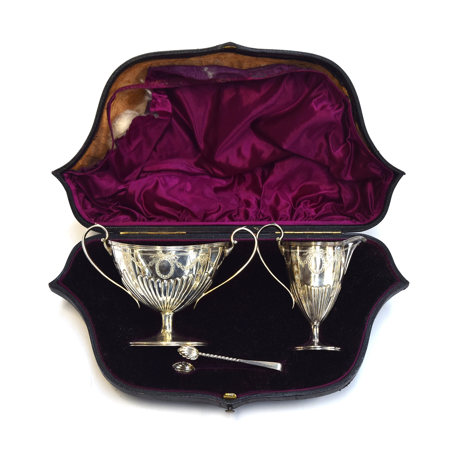 A late Victorian cased silver sugar bowl, milk jug, and tongs, each half reeded with engraved swags,