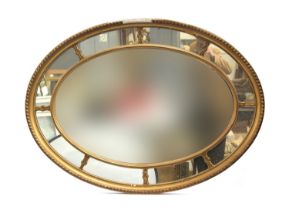 An early 20th century gilt gesso oval mirror, central bevelled plate, surrounded by eight further