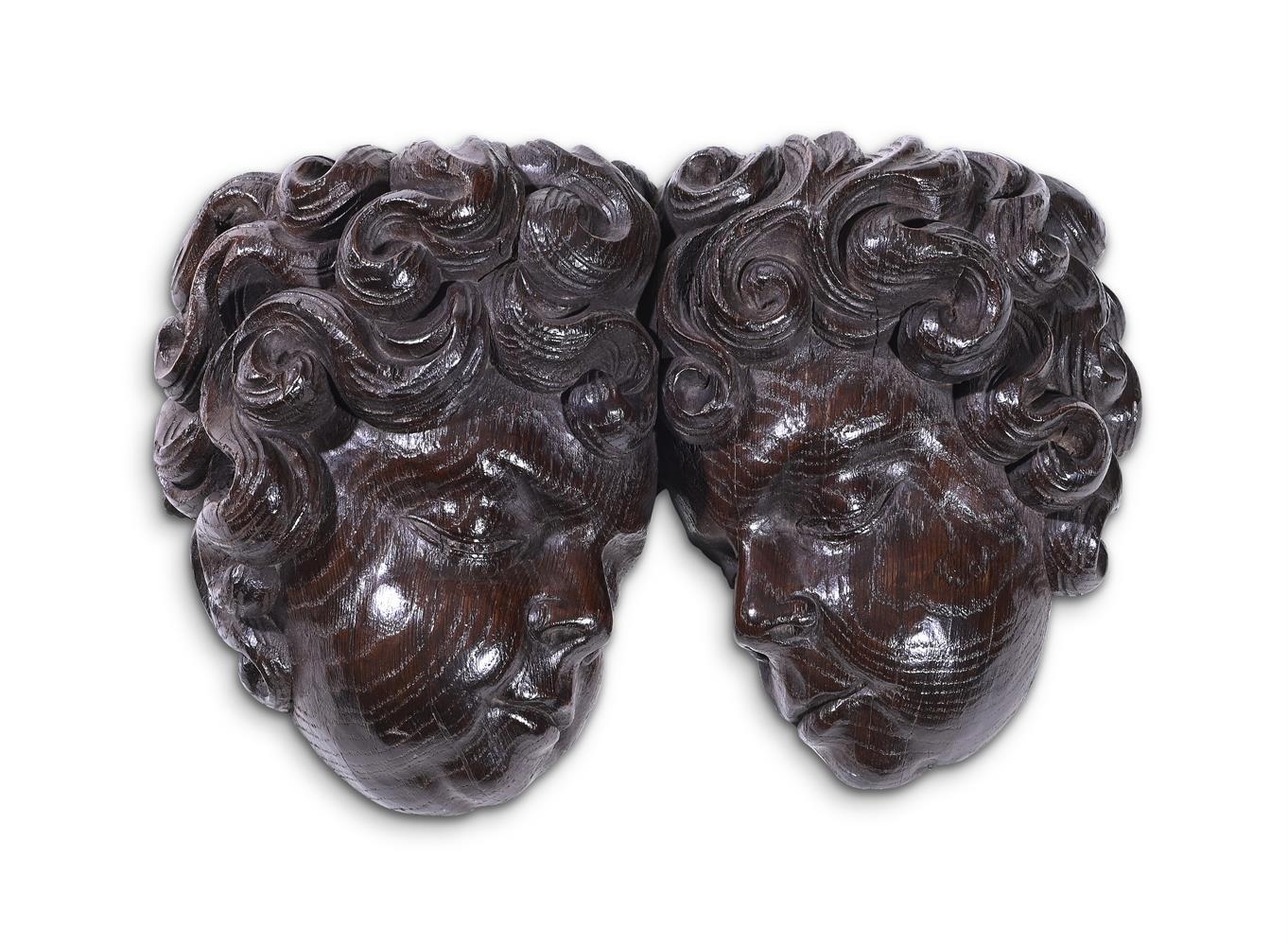 An early 20th century carved oak wall mount, modelled as two opposing tousled cherub heads, 39cm