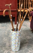 A floral ceramic stick stand containing five various walking sticks
