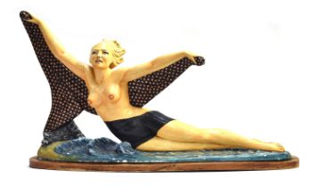 A polychrome painted plaster figure of a reclining nude holding her dotted shawl aloft, on a beach