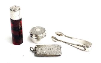 An engraved silver vesta case; a pair of sugar tongs; silver pill box and silver topped ruby glass