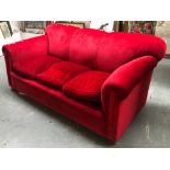 A large red velvet upholstered country house sofa, three feather filled cushions, on compressed