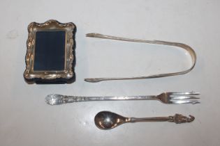 A small silver mounted photo frame; a pair of silver bright cut sugar tongs; a silver pickle fork