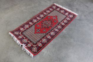 An approx. 5'3" x 2'6" red patterned rug
