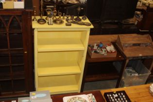 A yellow painted open fronted bookcase; an oak two tier tea trolley and a pine hanging plate rack