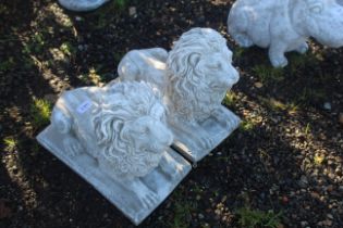 A pair of cast concrete garden ornaments in the form of small laying lions