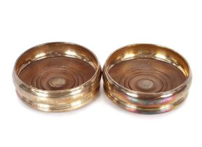 A pair of Elizabeth II silver coasters, with turned wooden bases having central monogram motifs,