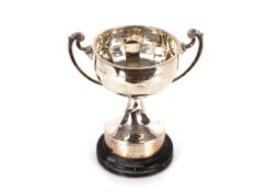 A silver trophy cup, having half fluted body decoration and scrolled handle, raised on a blackwood