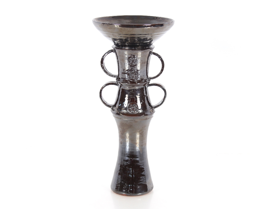 A dark lustre glazed Studio pottery candlestick, with ring handles and raised decoration, 33cm high