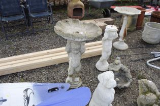 A concrete garden bird bath raised on cherub plint