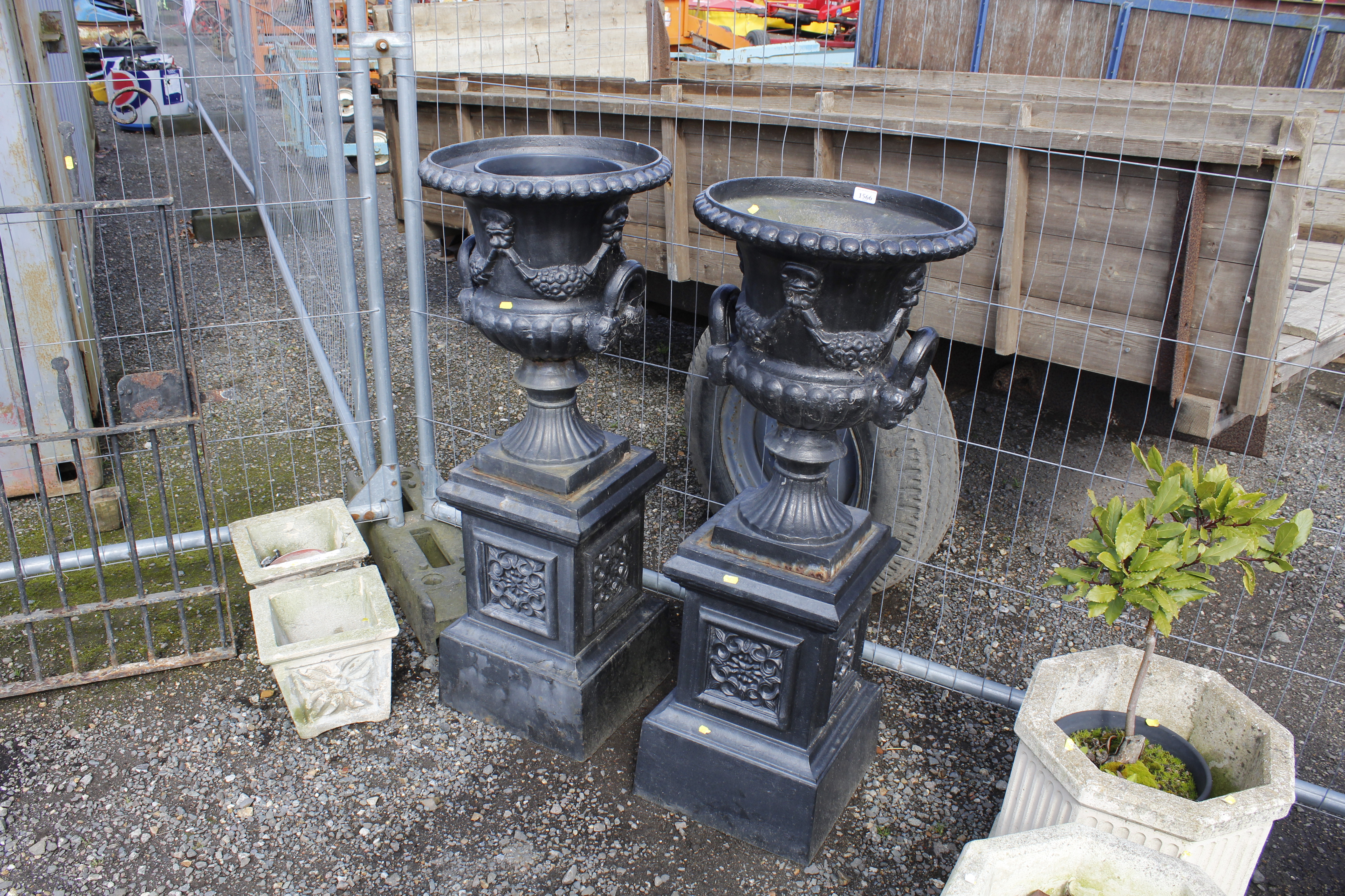 A pair of cast metal garden urns raised on plinths