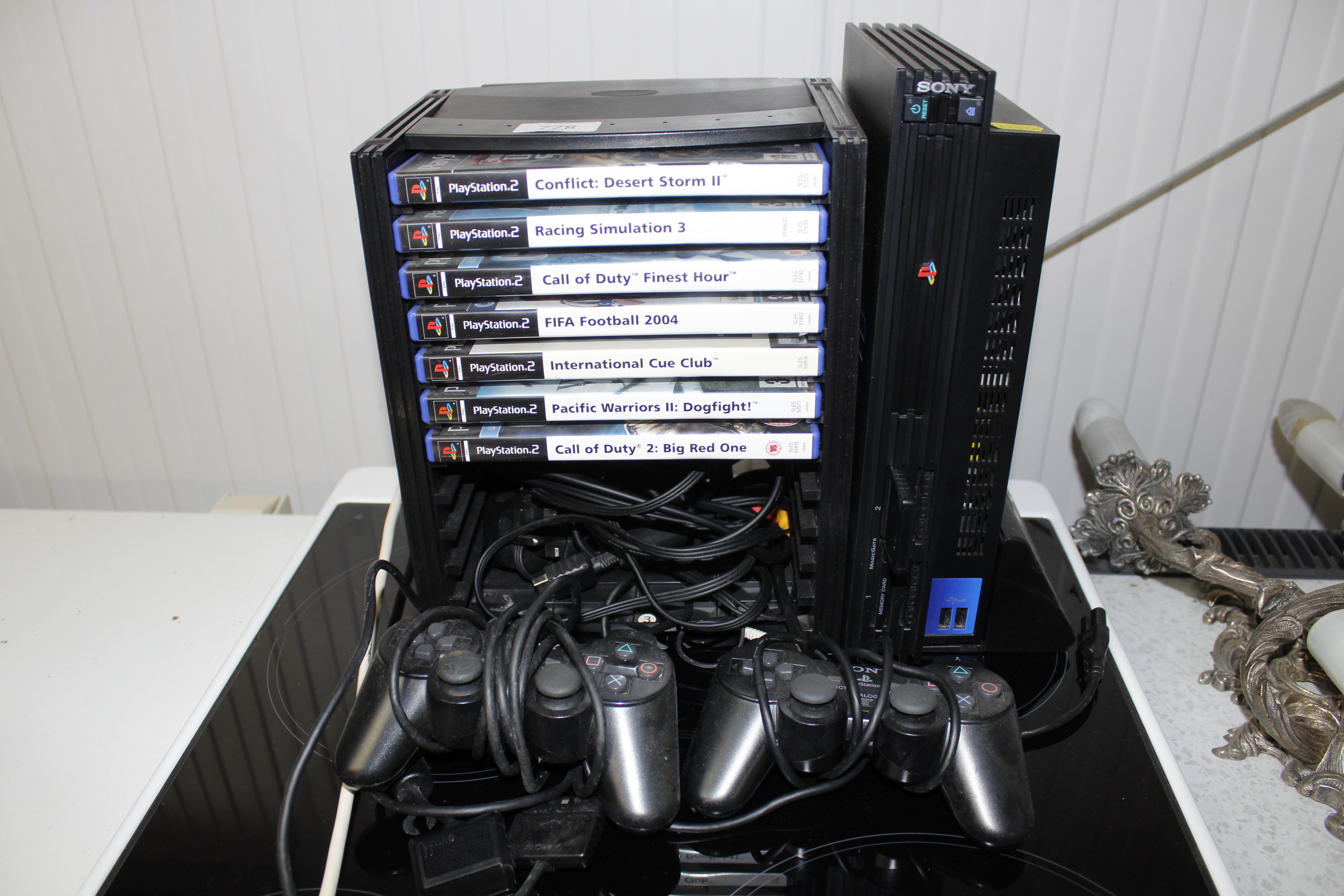 A PlayStation 2 with stand, remote controls and va
