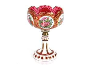 A 19th Century ruby glass overlaid pedestal bowl, the panels with profuse foliate decoration on gilt